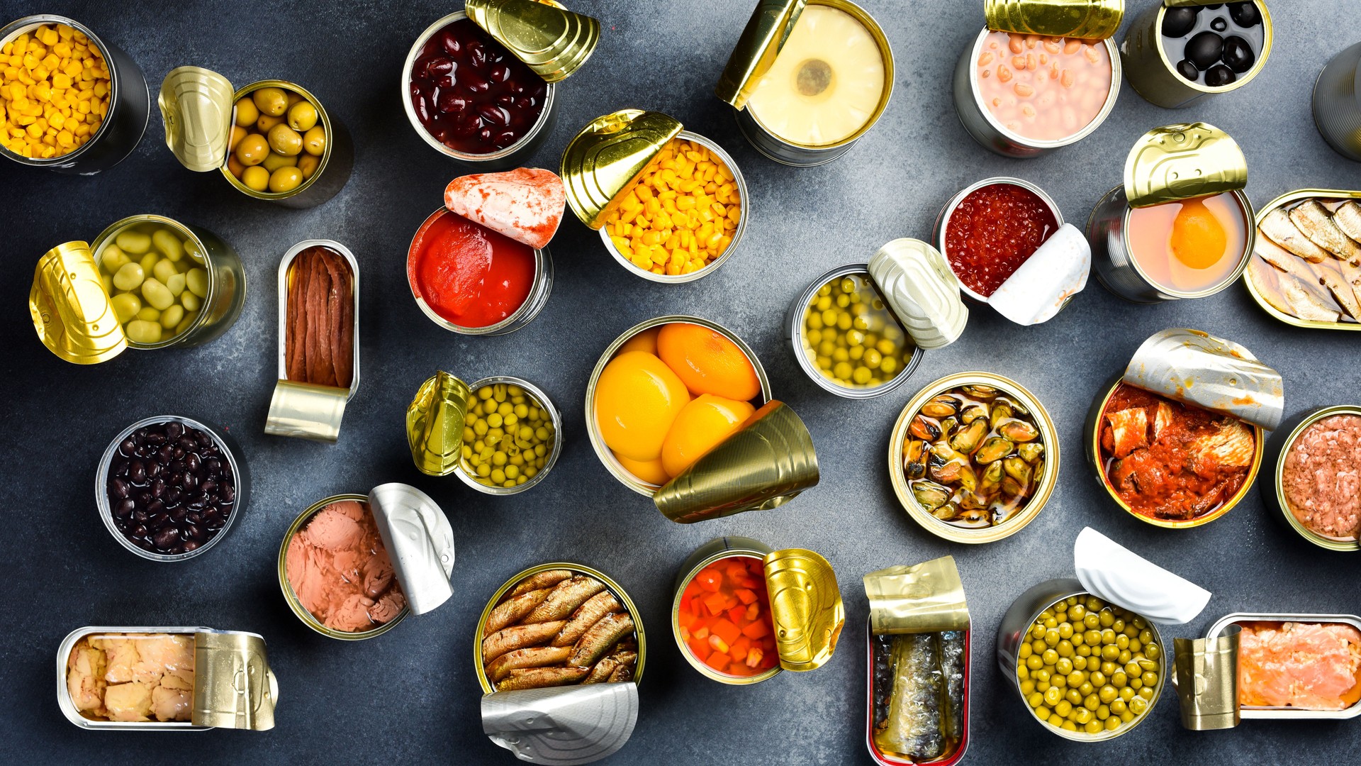 Food background in tin cans. Canned vegetables, beans, fish and fruits on a stone background. Food banner. Top view.